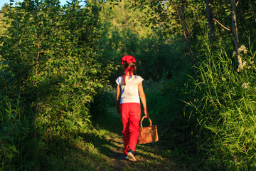 Young girl walking on a path through green woods carrying a birchbark basket