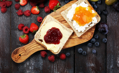 Toast bread with homemade strawberry jam and apricot marmalade on rustic table served with butter for breakfast or brunch