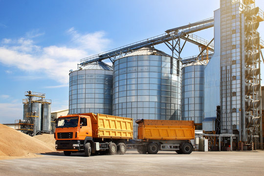 Agricultural silo truck of orange color on the territory of grain storage in sunny weather.