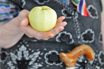 Ripe Apple in the hand of an elderly woman in a knitted vest for a walk. 90 years. Health and...