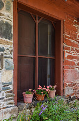 three pots of pink geraniums  in window of historic  red mill building 
