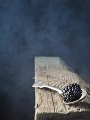 Fresh blackberry on vintage spoon and old piece of wood. Dark background. Shallow depth of field. Copy space.