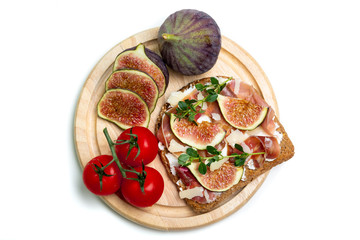 Top view of a toast with Parma ham, Parmesan cheese, fig slices, and thyme served on a wooden board with figs and cherry tomatoes