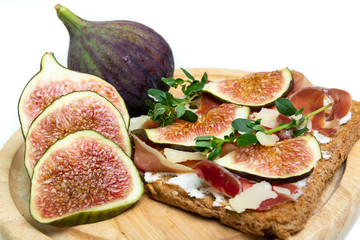 Close up of a toast with Parma ham, Parmesan cheese, fig slices, and thyme served on a wooden board with figs