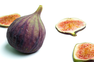Close up of a ripe purple fig surrounded by fig slices on white background