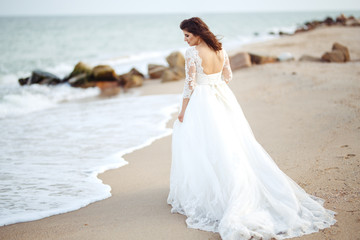 Fototapeta na wymiar A beautiful bride in a white wedding dress is walking along the beach. Waves near her dress. Beautiful sunset atmosphere, summer evening. Wedding concept.