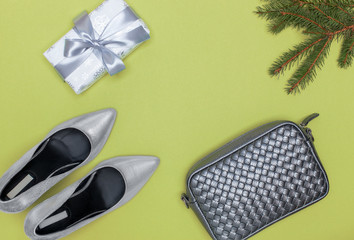 a view from above on a Christmas tree branch and a Christmas present, a New Year's gift, female silver stylish heels and a leather clutch, a waist bag with a silvery-gray weaving on a background