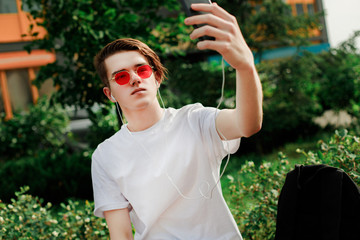 Young man in red glasses takes selfie in park