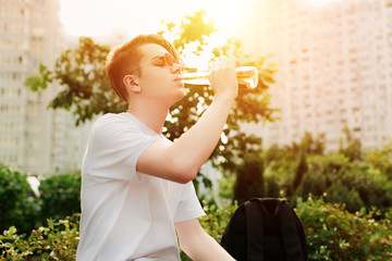 Young man drinks bottle of beer in park. Street Style, outdoor