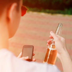 Young man with phone and bottle of beer in hands. Close view