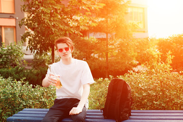 Young man sits and give a bottle of cider in park. Sunlight