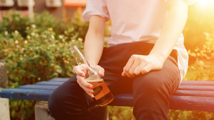 Young man sits with cidre bottle in hands. Close view. Sunlight