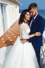 Naklejka premium Beautiful Bride and Groom enjoy each other on the background of the ocean. happy romantic young couple celebrating their marriage. Sexy stylish couple of lovers close up portrait. wedding concept.