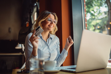 Portrait of blonde business woman shopping online while sitting in cafeteria