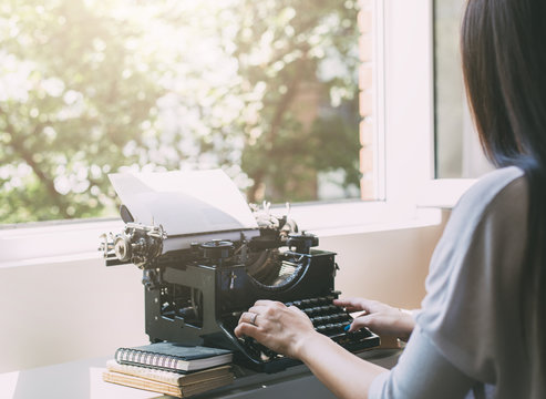 The girl writes a letter on the old typewriter.