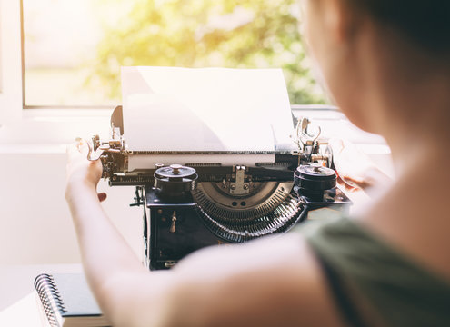 The girl writes a letter on the old typewriter.