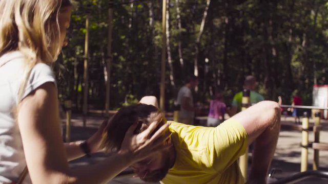 Young disable man in the park with his wife. The man is doing exercises on the parallel bars.