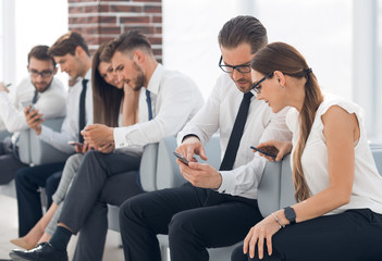 employees of the company using their smartphones sitting in the office lobby