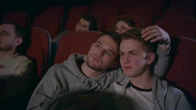 Couple gays embracing in movie theater. Homosexual men embracing in movie theatre. Gay couple watching movie in cinema