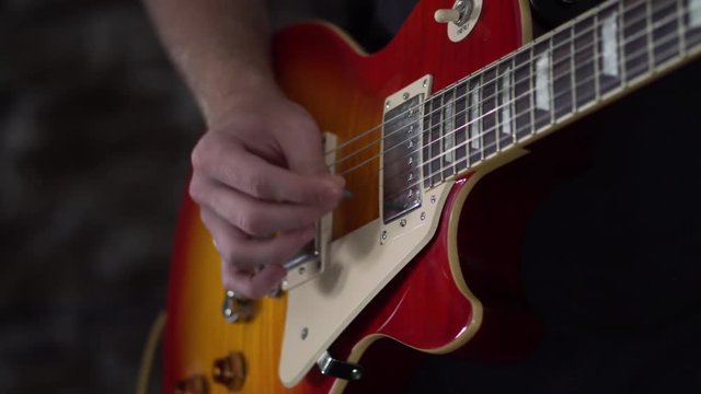 Man goes from picking his guitar to strumming out the last chord of the song with a Les Paul style guitar - close up shot on his right hand