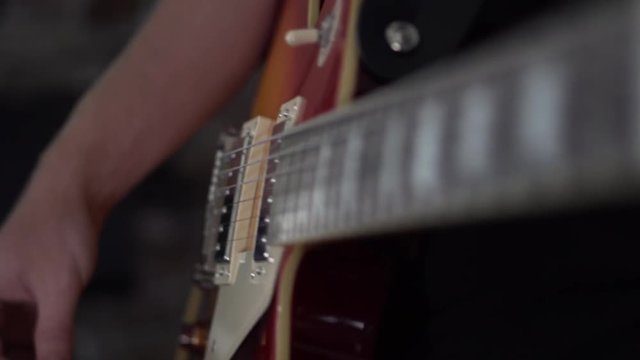 Man lightly strums a chord on his Les Paul style guitar - close up side shot of his strumming hand