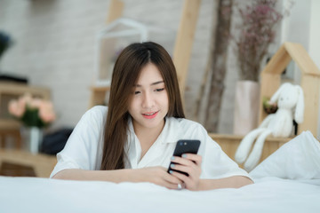 Beautiful Asian woman use of the smartphone sitting beside the bed.
