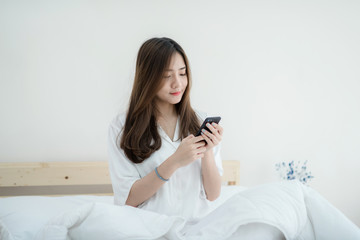 Beautiful Asian woman use of the smartphone sitting on bed