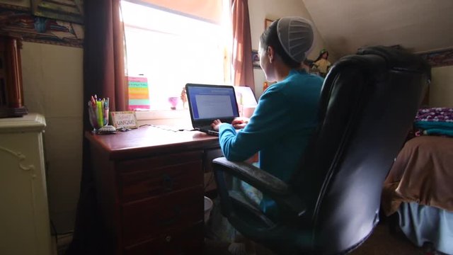 A young Mennonite woman smiling and talking as she works on a computer at her desk.