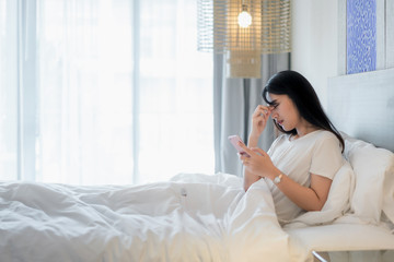 Asian woman in bed using mobile phone and feeling eye pain at bedroom in home.