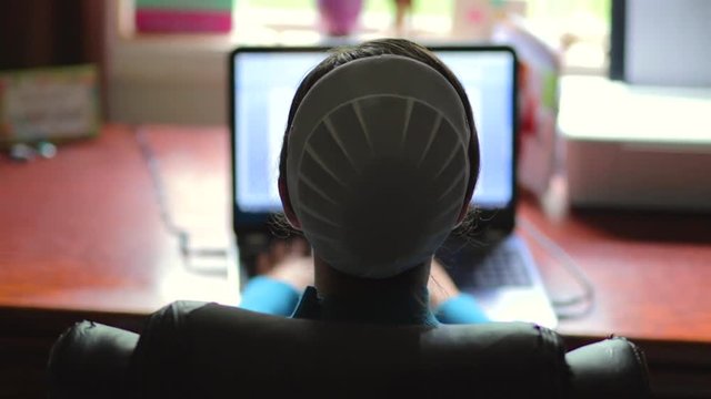 A young Mennonite woman comes into focus typing on a a computer in slow motion.