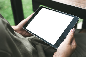 Mockup image of woman's hands holding black tablet pc with white blank screen while sitting in cafe with green nature background