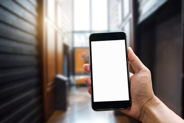 A man hand holding smart phone device in the bright office room interior.