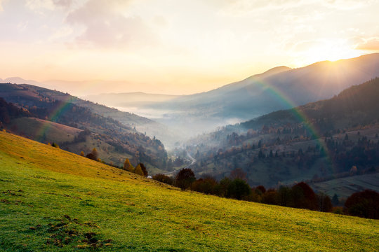 rainbow above the village in foggy valley. beautiful mountainous countryside at sunrise in autumn