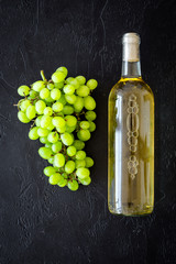 White wine in glass bottle near bunch of grapes on black background top view copy space