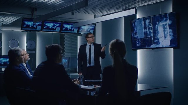 Special Agent in Charge Shows Satellite Surveillance Footage of the Car Getaway to a Team of Government Agents. GPS Tracking Fugitive in the Big Monitoring Room Full of Computers with Screens.