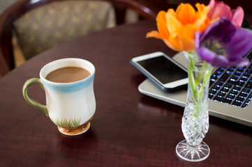 Coffee cup on desk with fresh flowers and laptop and mobile phone working freelance and business background