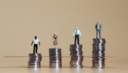 Miniature people standing on piles of coins.