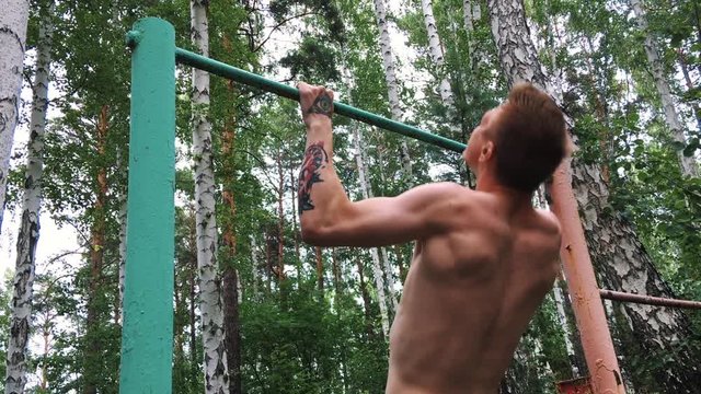Young attractive man is doing exercise on the parallel bars outdoors. Guy shirtless is engaged in amateur sports. Active lifestyle concept.