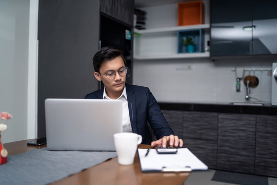 Asian Malay Man Working At Home With Laptop And Calculator