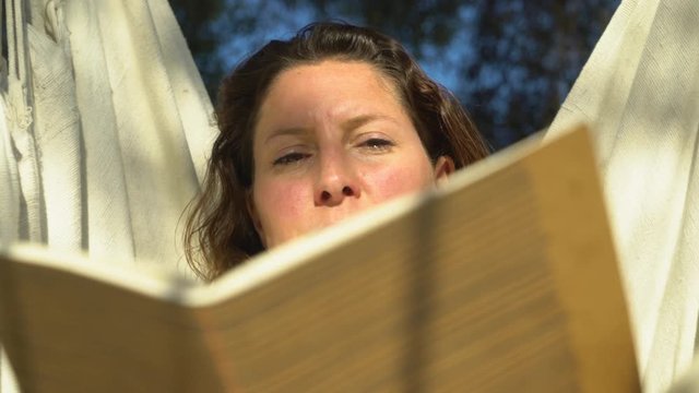 Woman relaxing in a hangmat chair and reading.