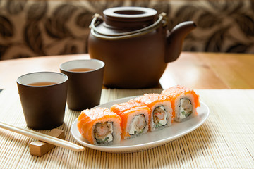 Sushi rolls with salmon and hot tea ceremony on table at home.Delivery of food at home.