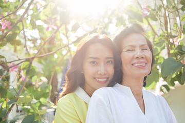 Cheerful Vietnamese smiling mother and daughter in sunny park