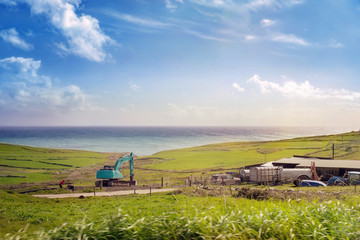 Ocean coast with a green excavator and a farm