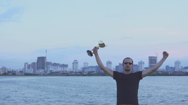 A young man with a cup in his hands at city evening. Concept as victory, success and champion.