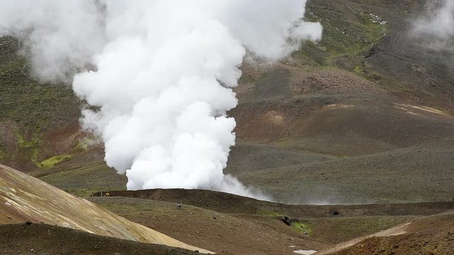 Viti Crater of Krafla caldera geothermal formation with mountains, snow during summer, industrial smoke steam vapor landscape view