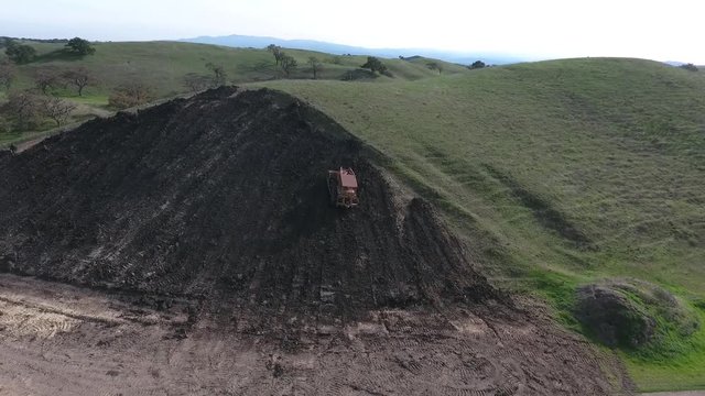 Bulldozer pushing dirt onto hill to rebuild its elegance