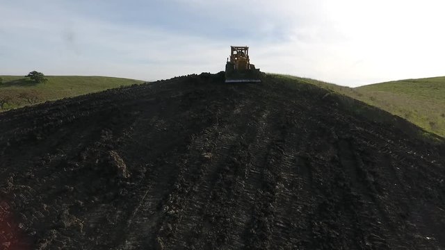 Bulldozer pushing dirt onto hill to rebuild its elegance