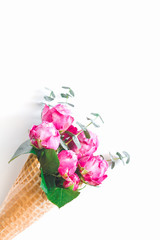 Creative minimalist composition with waffle cone with pink roses and eucalyptus inside on white background. The concept of gift and celebration. Flat lay, top view.