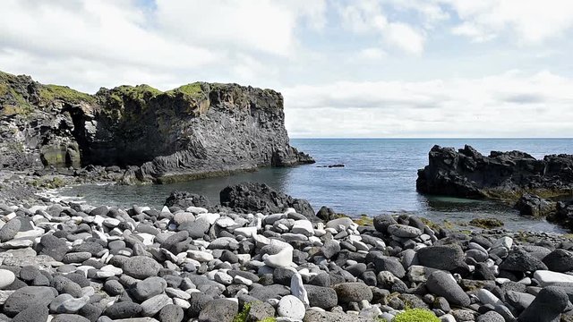Landscape trail hiking view of rocky beach in Hellnar, National park Snaefellsnes Peninsula, Iceland with ocean sea waves, green grass in summer day, cliff, clouds