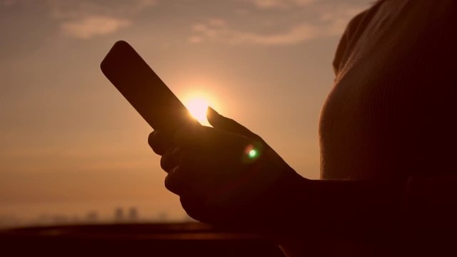 beautiful dusk time in the city. woman types on the cellular phone.
